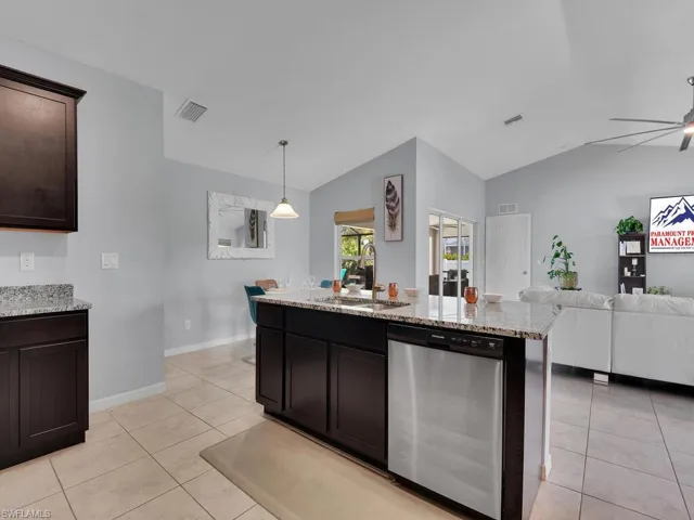 Kitchen featuring vaulted ceiling, dark brown cabinets, dishwasher, and decorative light fixtures