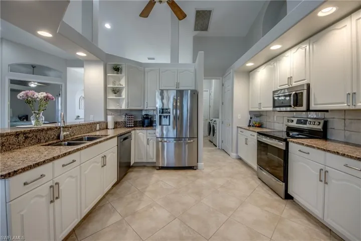 Kitchen with stainless steel appliances, washing machine and clothes dryer, light stone countertops, white cabinets, and recessed lighting
