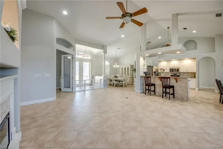 Living area featuring arched walkways, a glass covered fireplace, a ceiling fan, a chandelier, and french doors