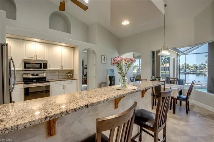 Kitchen with light stone counters, stainless steel appliances, a ceiling fan, a kitchen bar, and arched walkways