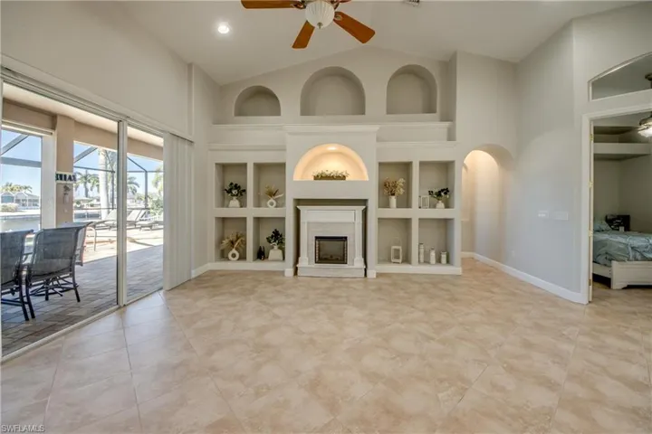 Unfurnished living room featuring a ceiling fan, built in features, lofted ceiling, a fireplace with raised hearth, and a sunroom
