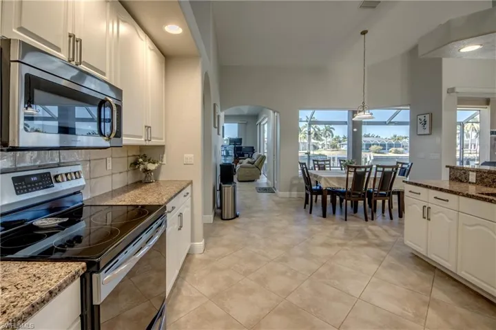 Kitchen with stainless steel appliances, arched walkways, dark stone counters, and white cabinetry