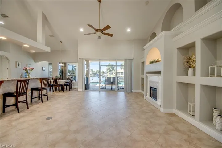 Living room with built in shelves, a glass covered fireplace, ceiling fan, a high ceiling, and recessed lighting