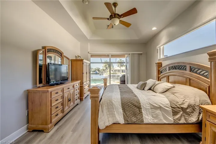 Bedroom featuring access to exterior, a ceiling fan, light wood finished floors, recessed lighting, and a tray ceiling