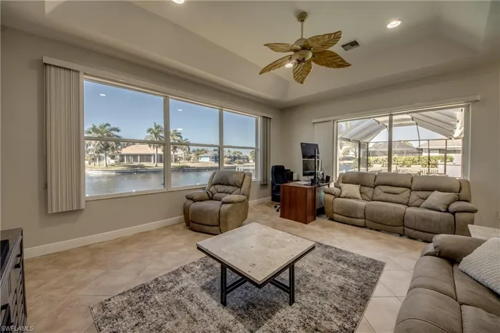 Living room featuring a ceiling fan, a sunroom, a tray ceiling, light tile patterned floors, and recessed lighting