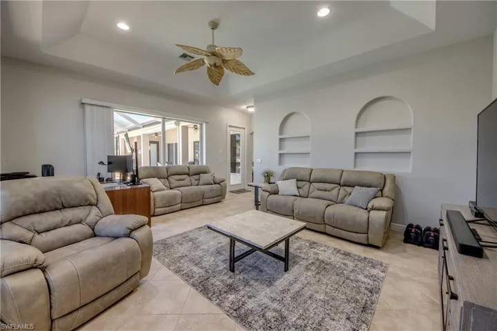 Living area featuring a raised ceiling, ceiling fan, built in features, recessed lighting, and light tile patterned floors