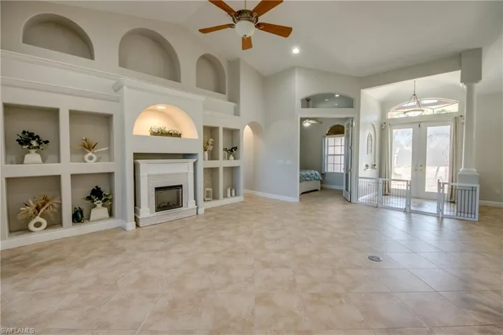 Unfurnished living room with built in shelves, a ceiling fan, french doors, a fireplace, and vaulted ceiling