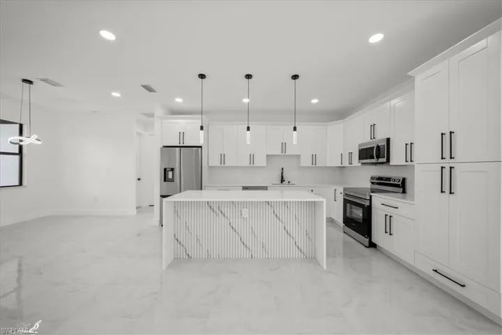 Kitchen with a center island, stainless steel appliances, decorative light fixtures, light marble finish flooring, and white cabinets