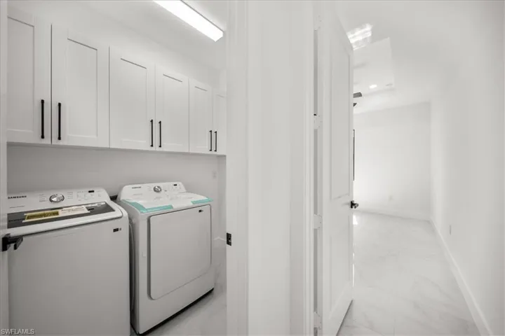 Laundry area with light marble finish flooring, cabinet space, and washing machine and clothes dryer