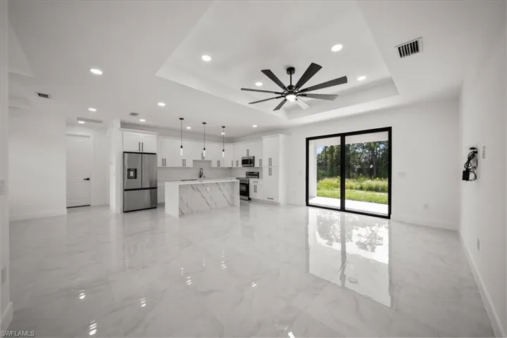 Unfurnished living room with a raised ceiling, light marble finish floors, recessed lighting, and a ceiling fan
