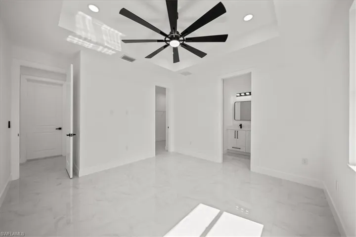 Unfurnished bedroom with light marble finish flooring, a raised ceiling, recessed lighting, a ceiling fan, and ensuite bathroom