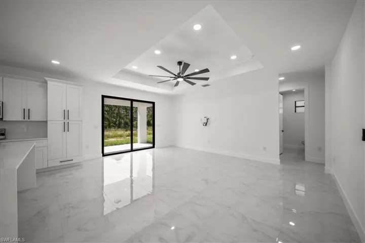 Unfurnished living room featuring a tray ceiling, light marble finish floors, recessed lighting, and a ceiling fan
