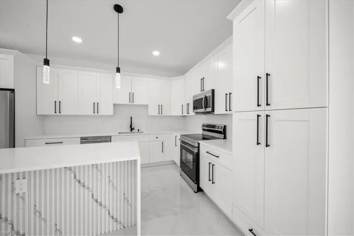 Kitchen with light marble finish flooring, stainless steel appliances, hanging light fixtures, light stone countertops, and white cabinets