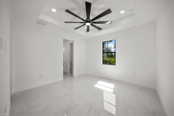 Empty room featuring a tray ceiling, light marble finish floors, recessed lighting, and a ceiling fan