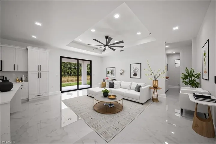 Living area featuring a raised ceiling, light marble finish flooring, ceiling fan, and recessed lighting
