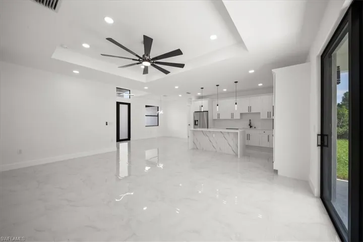 Unfurnished living room featuring a raised ceiling, light marble finish floors, recessed lighting, and a ceiling fan