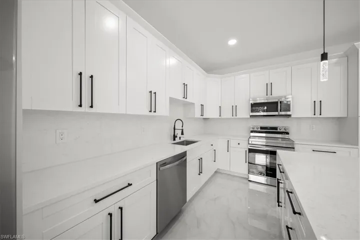 Kitchen featuring light marble finish flooring, appliances with stainless steel finishes, white cabinetry, pendant lighting, and recessed lighting