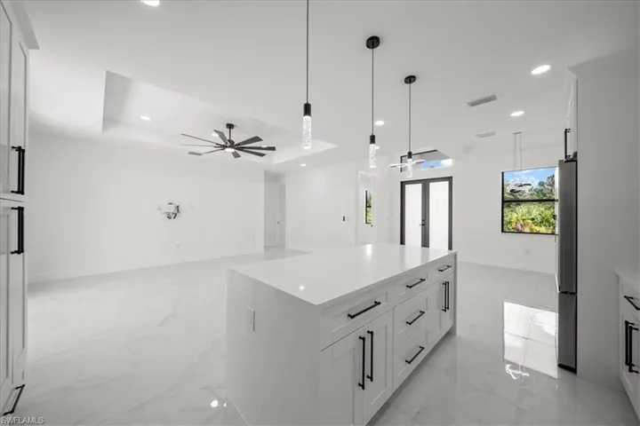 Kitchen featuring white cabinets, a raised ceiling, a kitchen island, pendant lighting, and recessed lighting