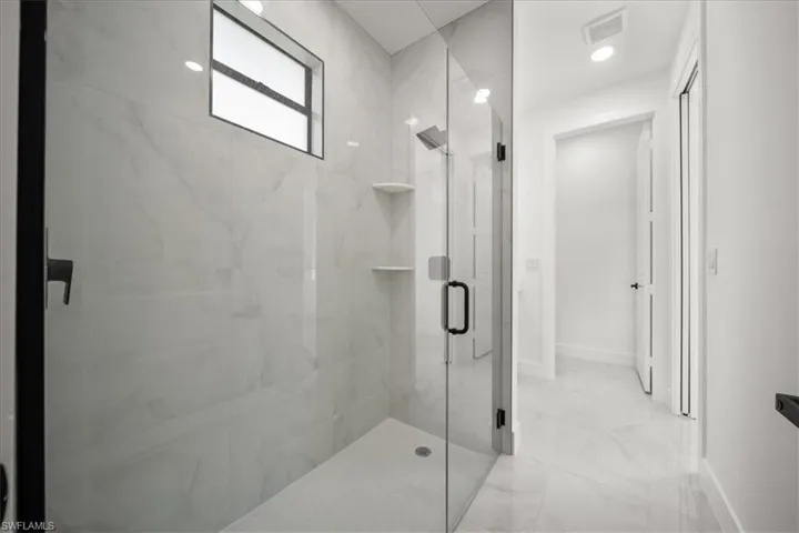 Full bath featuring a marble finish shower and light marble finish flooring