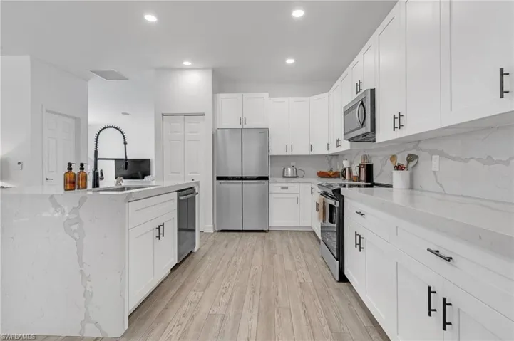 Kitchen featuring light stone countertops, stainless steel appliances, light hardwood / wood-style flooring, and white cabinets