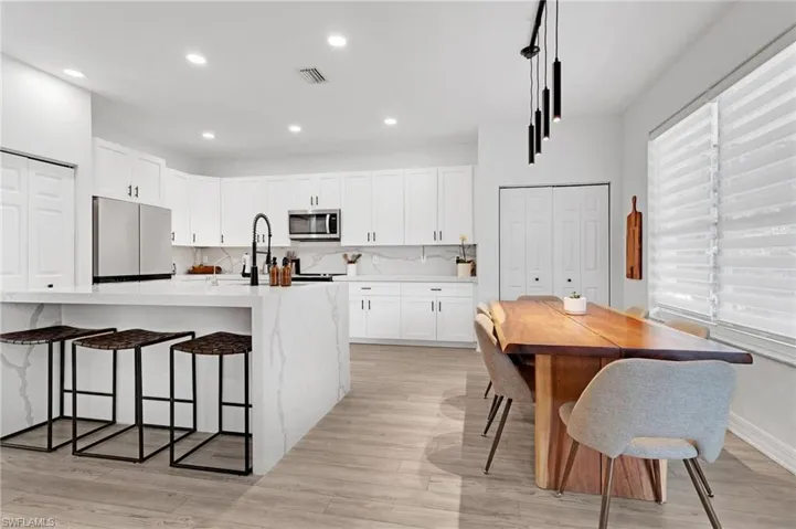 Kitchen featuring light hardwood / wood-style flooring, tasteful backsplash, white cabinetry, and appliances with stainless steel finishes