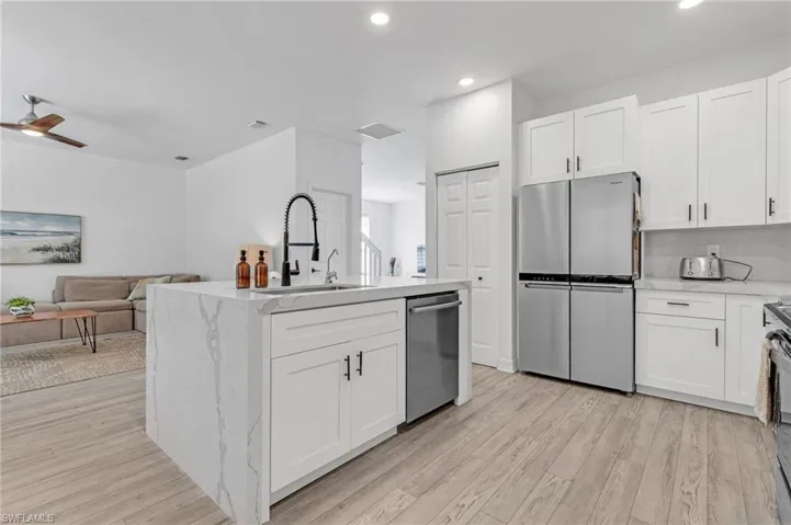 Kitchen with light hardwood / wood-style floors, ceiling fan, a kitchen island with sink, appliances with stainless steel finishes, and sink
