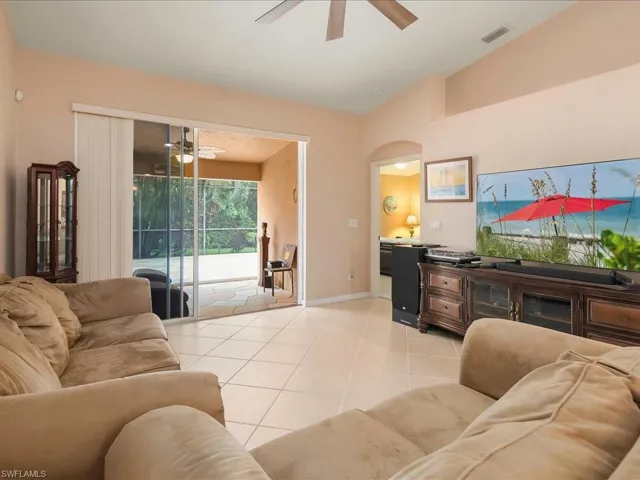 Living area with a ceiling fan, lofted ceiling, arched walkways, light tile patterned floors, and baseboards