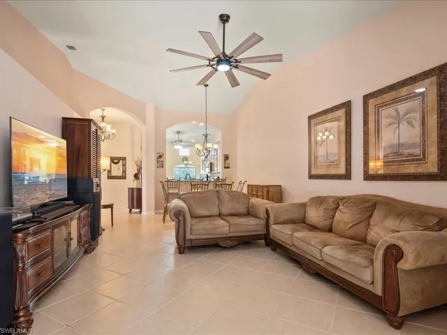 Living room featuring a chandelier, arched walkways, vaulted ceiling, light tile patterned floors, and a ceiling fan
