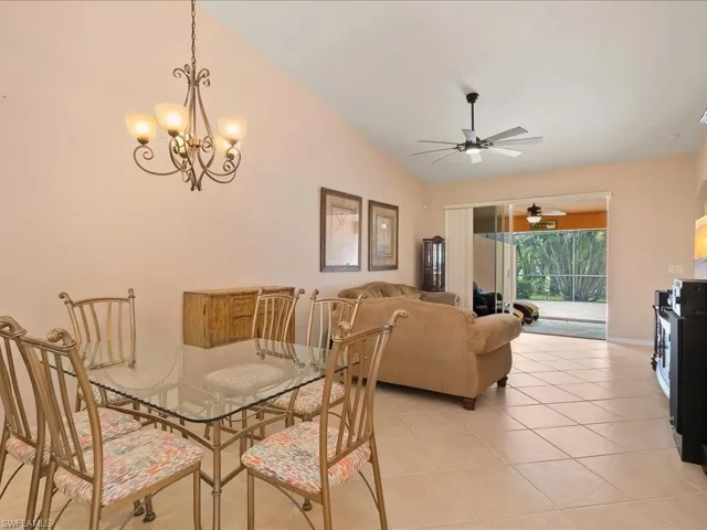 Dining space featuring lofted ceiling, light tile patterned floors, a chandelier, a ceiling fan, and baseboards
