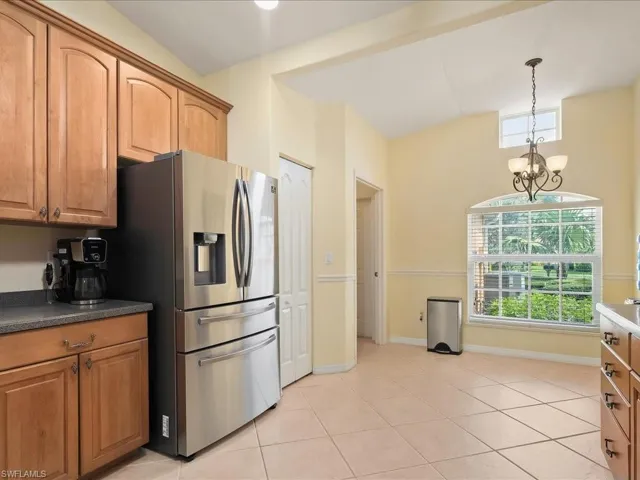 Kitchen with stainless steel fridge, light tile patterned floors, a chandelier, pendant lighting, and dark countertops