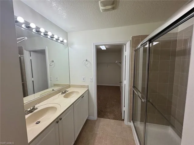Bathroom with tile patterned floors, vanity, a shower with door, and a textured ceiling