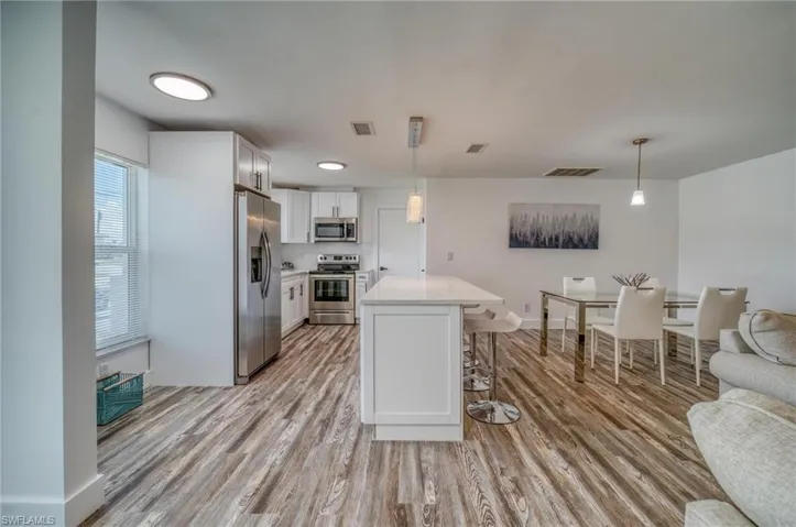 Kitchen featuring stainless steel appliances, a breakfast bar area, light wood-style floors, light countertops, and white cabinetry