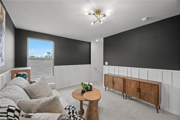 Living area featuring a chandelier, light colored carpet, and a wainscoted wall