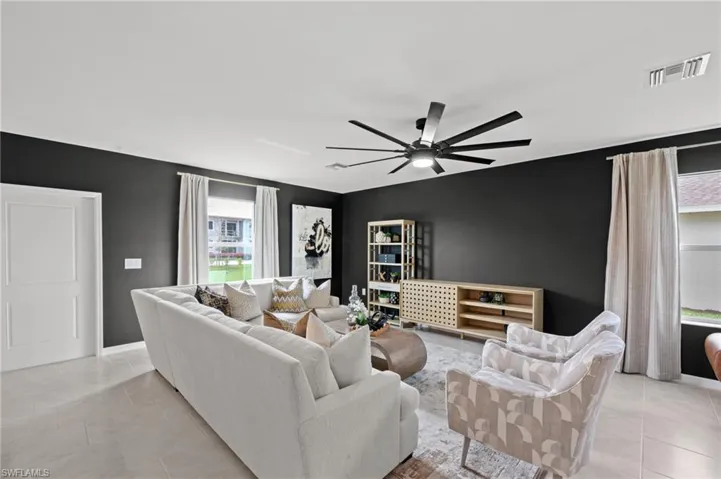 Living area with visible vents, light tile patterned floors, baseboards, an accent wall, and ceiling fan