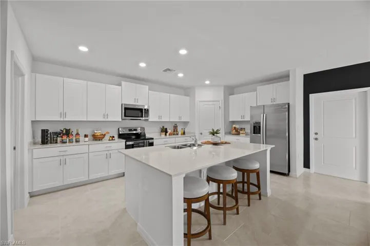 Kitchen featuring appliances with stainless steel finishes, a kitchen breakfast bar, white cabinetry, recessed lighting, and a center island with sink