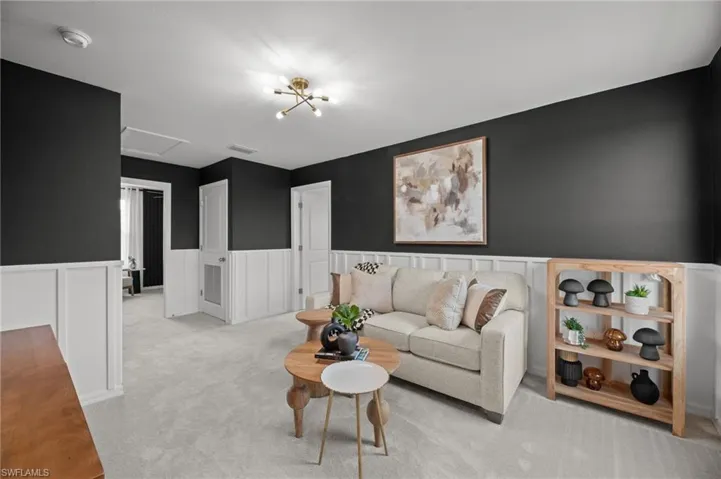 Living area with visible vents, a decorative wall, attic access, wainscoting, and light carpet