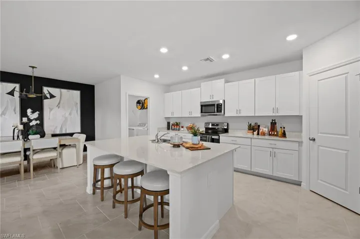 Kitchen with a breakfast bar, white cabinetry, visible vents, a center island with sink, and appliances with stainless steel finishes