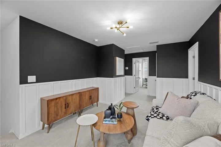 Living room with light carpet, attic access, visible vents, and a wainscoted wall
