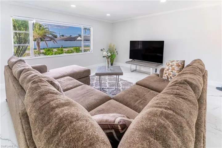 Living room featuring marble look tiles, crown molding, and recessed lighting
