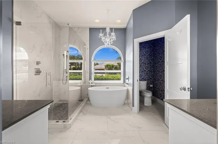 Spa-inspired primary bathroom featuring updated tile, a frameless glass shower, and beautiful arched windows that fill the space with natural light.
