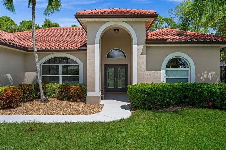 Beautiful curb appeal with a manicured lawn, mature tropical landscaping, and an inviting covered entry.
