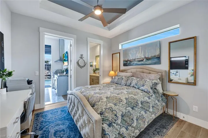 Bedroom featuring a raised ceiling, light wood finished floors, ceiling fan, and ensuite bath