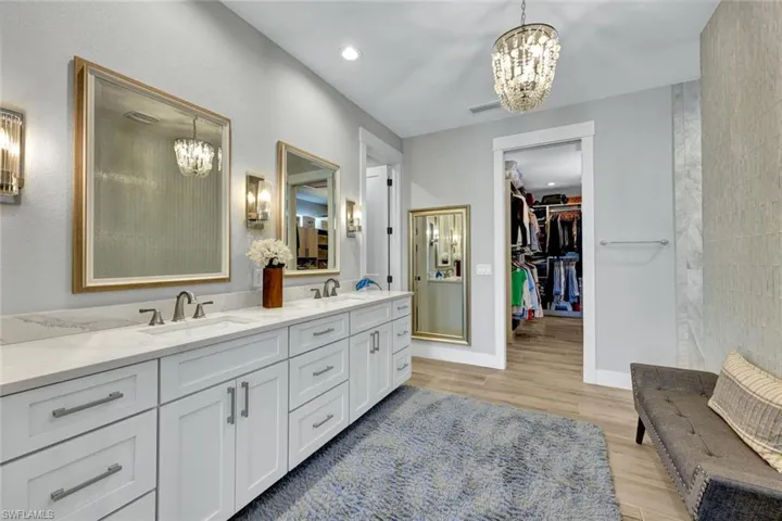 Full bath with a chandelier, light wood finished floors, double vanity, recessed lighting, and a walk in closet