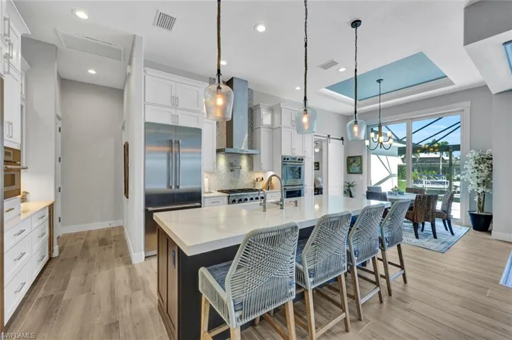 Kitchen featuring white cabinets, backsplash, light wood finished floors, decorative light fixtures, and light stone counters