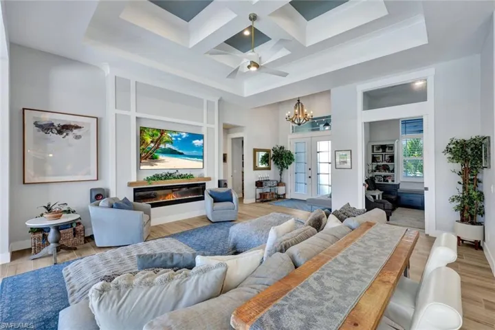 Living area with a chandelier, a glass covered fireplace, light wood-style flooring, french doors, and coffered ceiling