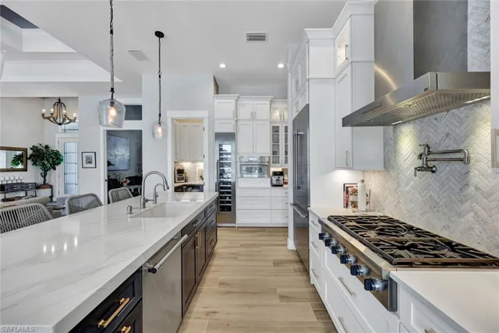 Kitchen with white cabinetry, decorative backsplash, wall chimney range hood, and recessed lighting