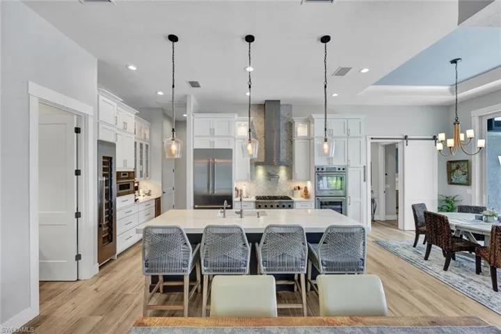 Kitchen with a barn door, decorative backsplash, decorative light fixtures, white cabinetry, and recessed lighting