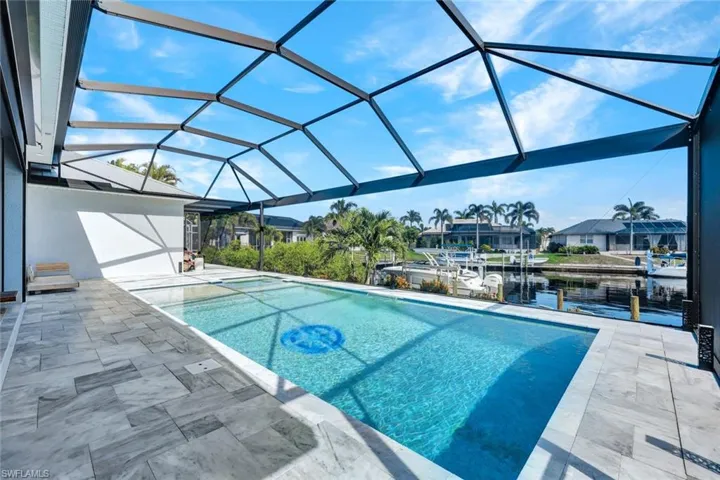 Outdoor pool with a sunroom, a water view, a patio, and glass enclosure