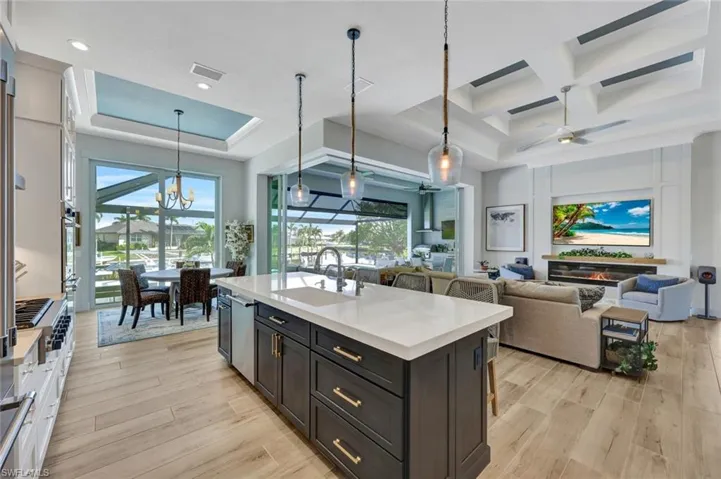 Kitchen with decorative light fixtures, a breakfast bar, light stone countertops, healthy amount of natural light, and coffered ceiling