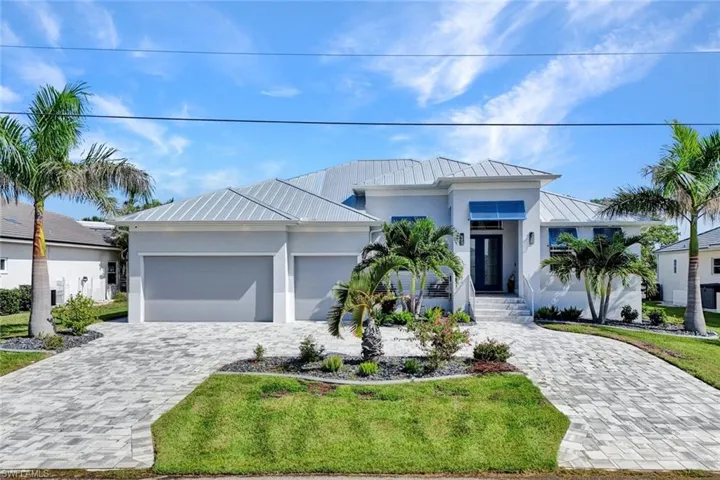 View of front of home with a standing seam roof, a metal roof, stucco siding, and decorative driveway